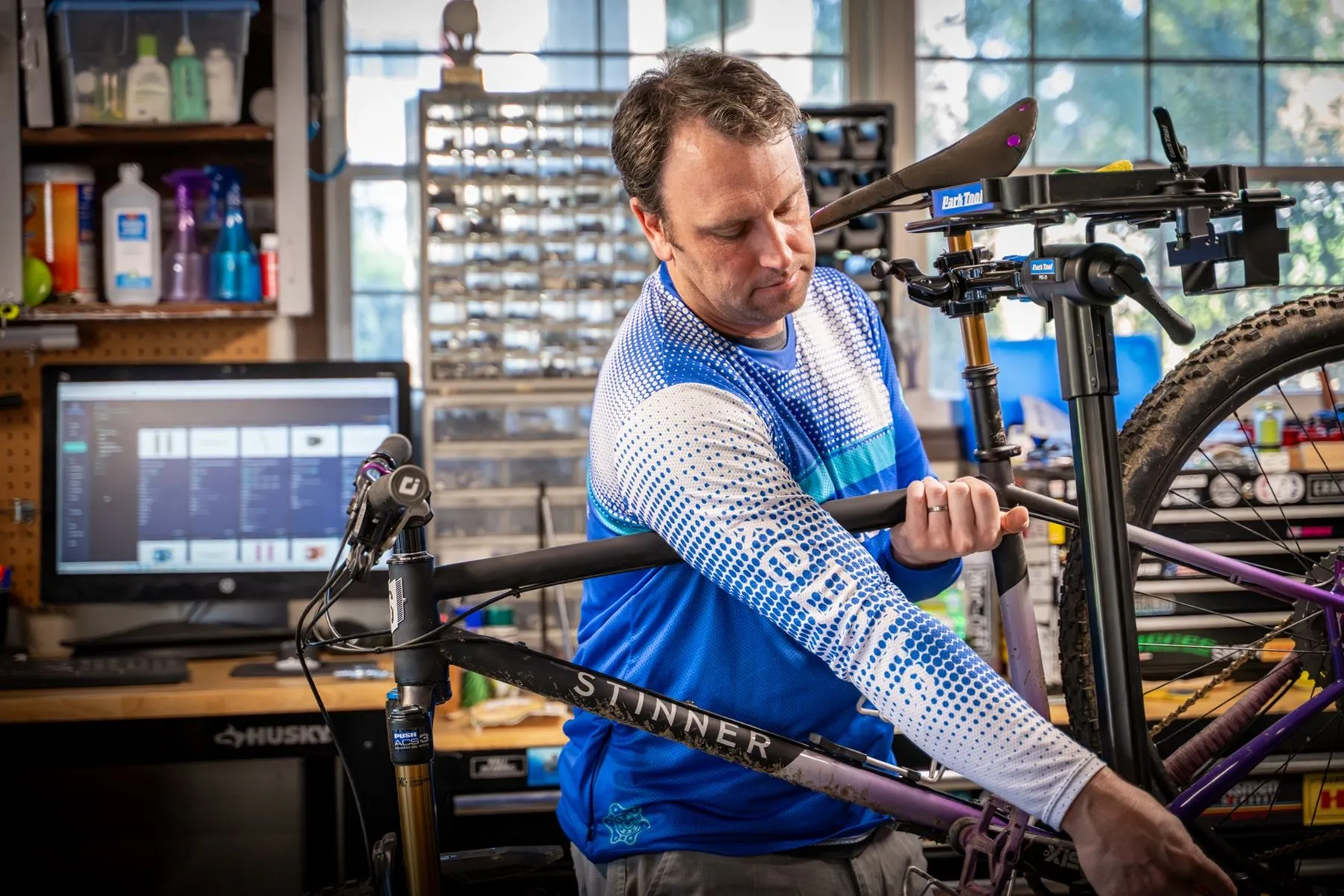 Rider working on parts at a home workshop bench, mountain bikes behind